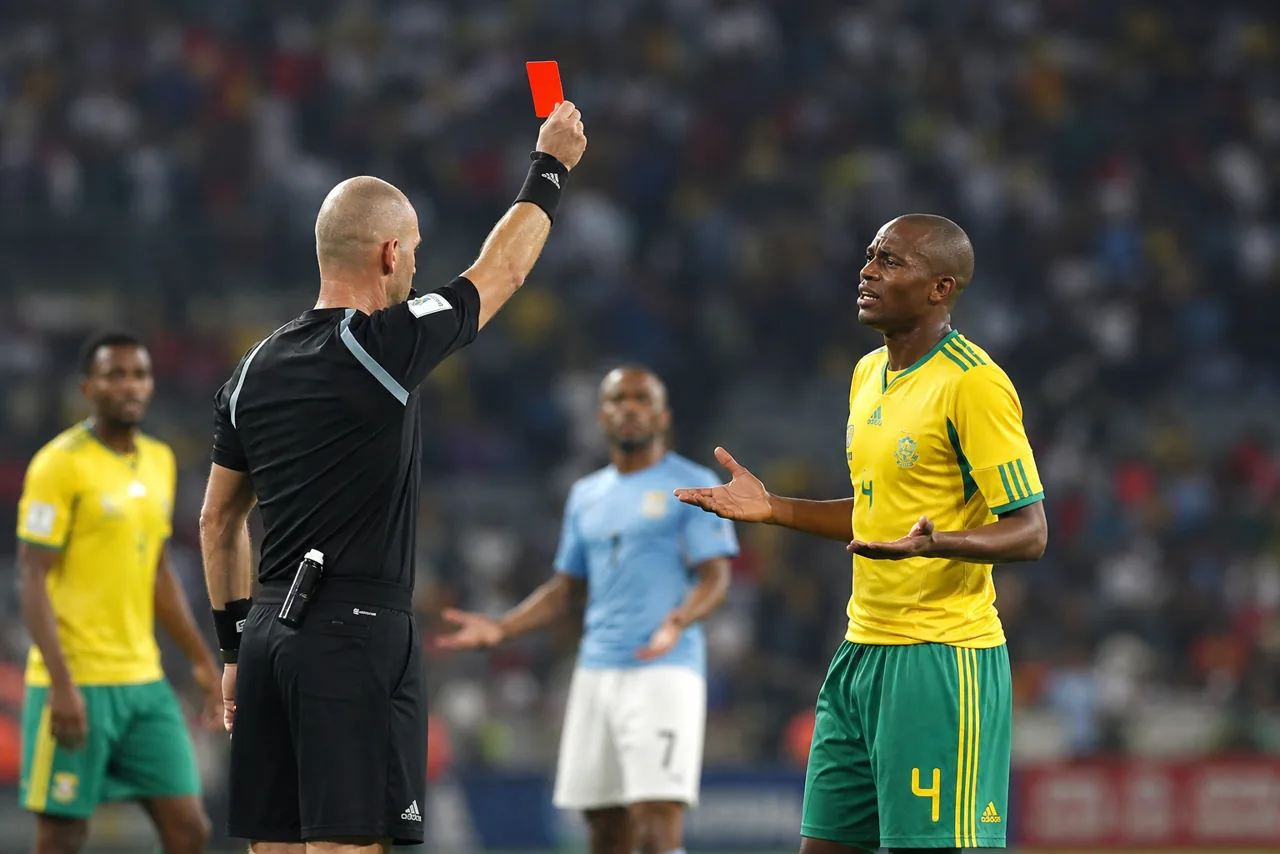 AI-foto van een WK-stadionmoment waarop een scheidsrechter een rode kaart toont aan een speler van Zuid-Afrika, met andere spelers op de achtergrond.