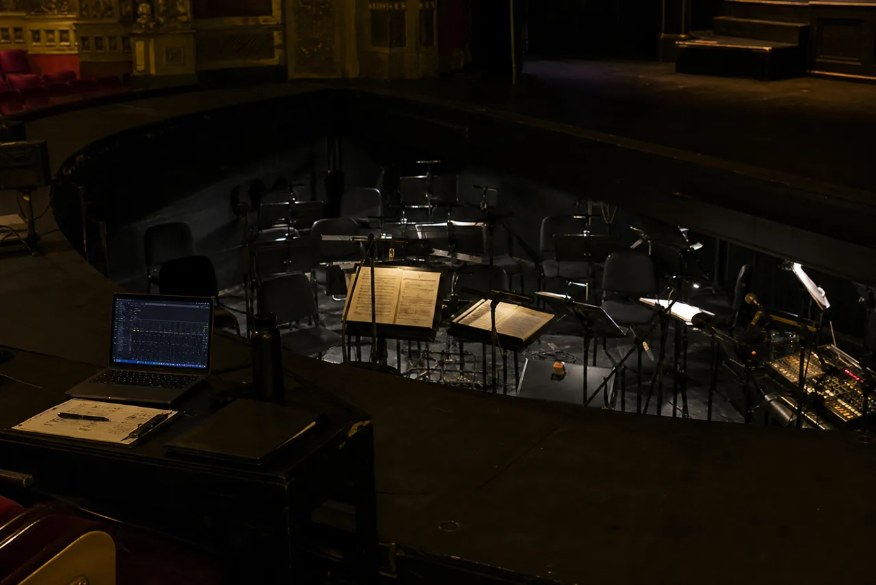 Een lege orkestbak met muziekstandaards en een technische desk in een theater.